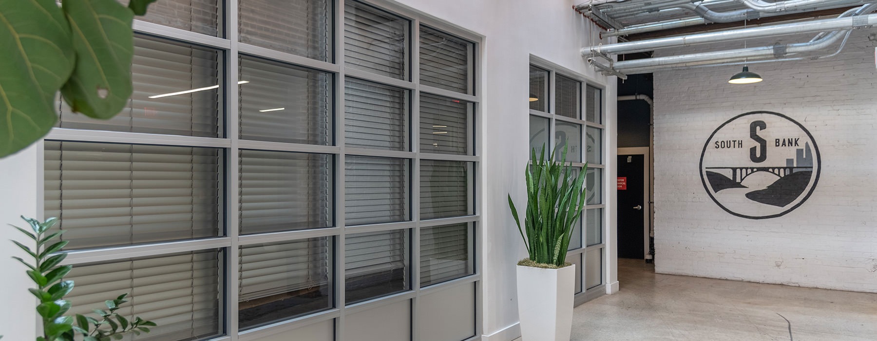 a hallway with windows plants and a white brick wall